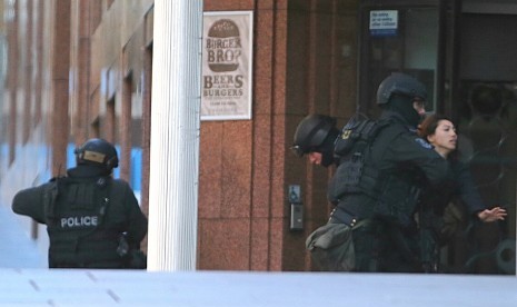  Sejumlah polisi bersenjata lengkap mengamankan seorang wanita yang berhasil melarikan diri dari penyanderaan di sebuah kafe di Sydney, Senin (15/12). (AP/Rob Griffith)