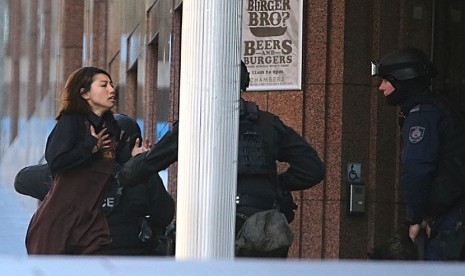  Sejumlah polisi bersenjata lengkap mengamankan seorang wanita yang berhasil melarikan diri dari penyanderaan di sebuah kafe di Sydney, Senin (15/12). (AP/Rob Griffith)