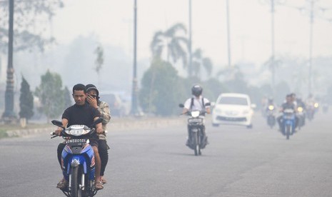  Pengendara sepeda motor tanpa mengenakan masker pelindung pernapasan saat melintasi Jalan Yos Sudarso yang diselimuti kabut asap kebakaran hutan dan lahan di Pekanbaru, Riau, Senin (27/7).  (Antara/Rony Mularman)