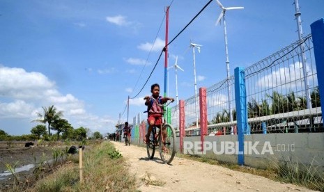 Pelajar melintas berlatar kincir angin Energi Mandiri Tenaga Surya dan Angin ( E Mas Bayu), Kampug Laut, Cilacap, Jawa Tengah (ilustasi). 