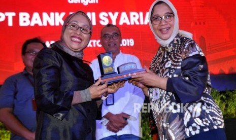 Direktur Sales Telkomsel Ririn Widaryani (kedua kiri) dan Direktur Bisnis SME & Komersial BNI Syariah Dhias Widhiyati (kanan) bertukar cinderamata usai penandatanganan MoU, disela Telkomsel Umrah Fair, di Jakarta, Rabu (30/10/2019).