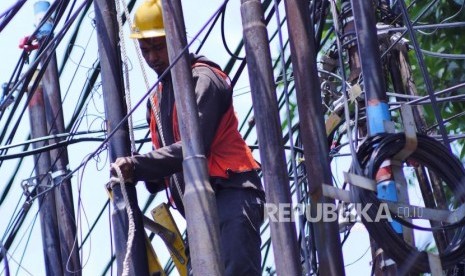 Seorang pekerja sedang mengikatkan tali katrol dalam upaya mencabut tiang kabel optik untuk dimasukkan ke dalam tanah di Jalan Raya Kemang, Jakarta Selatan, Senin (18/11/2022).