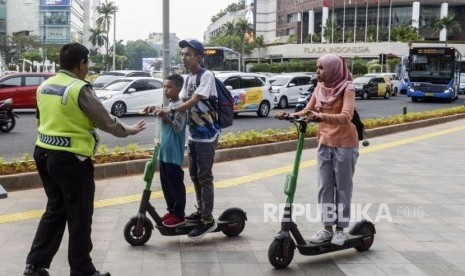 Anggota kepolisian menghentikan pengguna skuter listrik yang melintas di jalan MH Thamrin, Jakarta, Ahad (24/11).