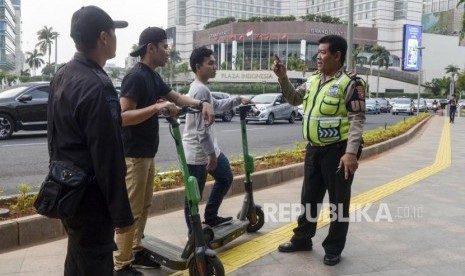 Anggota kepolisian memberi himbauan kepada pengguna skuter listrik yang melintas di jalan MH Thamrin, Jakarta, Ahad (24/11).