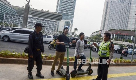 Anggota kepolisian memberi himbauan kepada pengguna skuter listrik yang melintas di jalan MH Thamrin, Jakarta, Ahad (24/11).