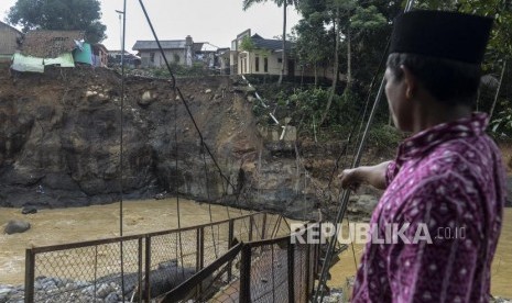 Seorang warga memperlihatkan jembatan yang putus akibat banjir bandang dan longsor (ilustrasi)