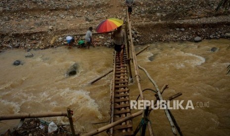 Warga menyeberangi jembatan kayu di Kampung Muara, Desa Banjarsari, Kecamatan Lebak Gedong, Banten, Senin (13/1).