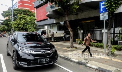 Warga melintas di dekat mobil yang terparkir di Jalan Gajah Mada, Jakarta, Kamis (20/2).