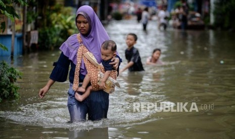 Warga berjalan melintasi area yang terendam banjir di Jalan Satria IV, Kelurahan Jelambar, Jakarta Barat, Selasa (25/2).