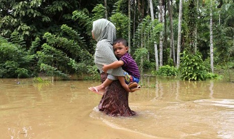  Seorang warga mengendong anaknya saat melintasi banjir di Desa Buket Liteung, Kecamatan Langkahan, Aceh Utara, Aceh. (ilustrasi)