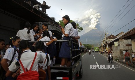  Pelajar berangkat ke sekolah dengan latar pemandangan Gunung Agung saat memuntahkan asap dan abu vulkanis di Karangasem, Bali, Selasa (28/11).  