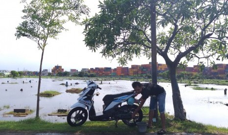 Seorang warga Gang Lengkong mencuci sepeda motor di Tempat Pemakaman Umum (TPU) Semper, Cilincing, Jakarta Utara yang terendam banjir, Kamis (6/12).