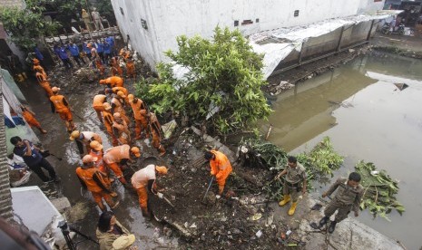 Petugas PPSU membersihkan lumpur yang menggenangi jalan pemukiman warga karena tanggul aliran Kali Pulo jebol di Kelurahan Jati Padang, Kecamatan Pasar Minggu, Jakarta, Senin (14/1/2019).