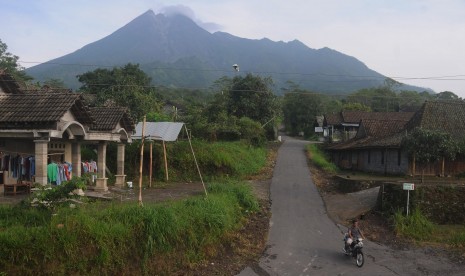 Warga melintas di jalan desa dengan berlatar belakang Gunung Merapi. 