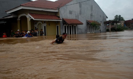 Warga berusaha menyebrangi jalan yang tergenang banjir di Kecamatan Manggala, Makassar, Sulawesi Selatan, Rabu (23/1/2019).