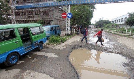 Penumpang melewati kubangan air di jalan yang rusak di Terminal Bubulak, Kota Bogor, Jawa Barat, Jumat (15/2/2019).