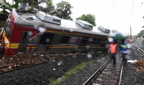 Petugas melintasi KRL Commuter Line 1722 yang anjlok di pintu perlintasan Kebon Pedes, Tanah Sareal, Kota Bogor, Jawa Barat, Ahad (10/3/2019).