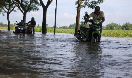 Warga mendorong motor yang mogok saat melintasi banjir di Desa Glundengan, Wuluhan, Jember, Jawa Timur