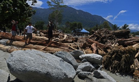 Sejumlah warga melintas di antara bongkahan kayu dan batu yang terbawa arus banjir bandang di Kampung Hinekomba, Sentani, Jayapura, Papua, Sabtu (23/3/2019).