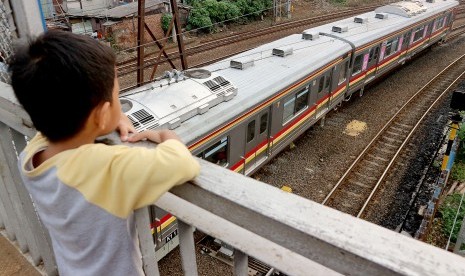 Seorang bocah mengamati rangkaian kereta rel listrik (KRL) Commuterline melintas di kawasan Stasiun Jatinegara, Jakarta, Selasa (9/4/2019).