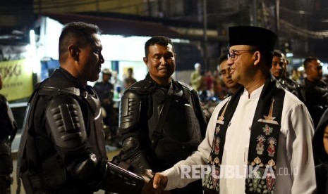 Gubernur DKI Jakarta Anies Baswedan (kanan) menjabat tangan petugas polisi yang bertugas mengamankan kawasan sekitar Kantor Bawaslu RI di Jalan Wahid Hasyim, Jakarta Pusat, Jumat (24/5/2019) malam.