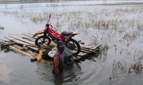 Seorang petani membawa sepeda motornya dengan rakit melintasi banjir yang merendam sawah di Desa Puduria, Konawe, Sulawesi Tenggara, Rabu (19/6/2019).