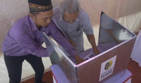 Petugas membantu warga menggunakan hak pilih dalam Pemilihan Kepala Desa (Pilkades).