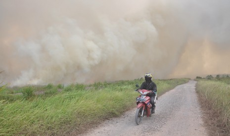 Warga melintas dengan kendaraanya saat terjadi kebakaran lahan gambut di Desa Pulau Semembu, Indralaya Utara, Ogan Ilir, Sumatra Selatan, Senin (5/8/2019).