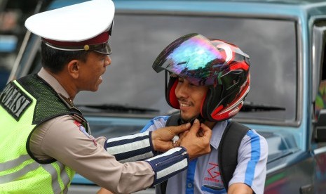 Ilustrasi tertib lalu lintas. Foto: Polantas membantu mengencangkan tali helm pengendara sepeda motor saat dilakukan kampanye 