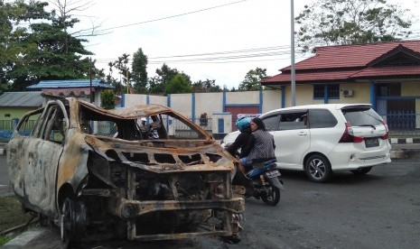 Warga melintas di samping bangkai mobil yang terbakar di Manokwari, Papua Barat, Selasa (20/8/2019).