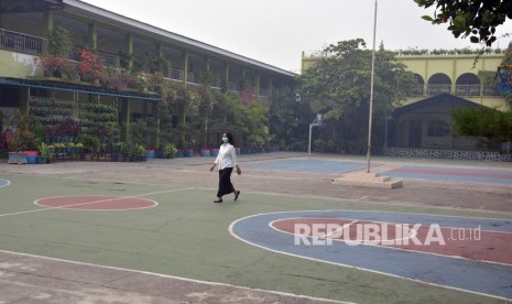 Seorang guru mengenakan masker melintasi halaman SD Santa Maria yang kosong karena sekolah diliburkan di Kota Pekanbaru, Riau, Rabu (11/9/2019). 