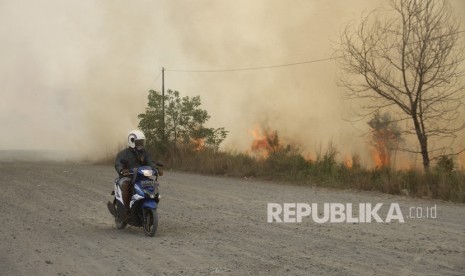 Pengendara roda dua melintas di samping api yang membakar lahan gambut di Jalan Tegal Arum kawasan Syamsudin Noor, Banjarbaru, Kalimantan Selatan, Jumat (13/9/2019).