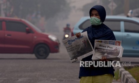 Seorang penjual koran mengenakan masker medis saat berjualan di tengah asap kebakaran hutan dan lahan (Karhutla) yang makin pekat menyelimuti Kota Pekanbaru, Riau, Jumat (13/9/2019). 