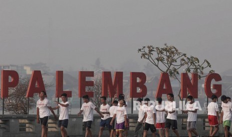 Sejumlah warga beraktivitas dengan latar belakang kabut asap yang menyelimuti kawasan Pelataran Benteng Kuto Besak Palembang, Jumat (13/9/2019). 