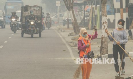 Petugas Kebersihan mengenakan masker ketika menyapu jalan saat kabut asap dampak kebakaran hutan dan lahan menyelimuti Kota Pekanbaru, Riau.