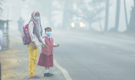 Seorang siswa bersama orang tuanya mengenakan masker saat menunggu angkutan umum, di Palembang, Sumatera Selatan, Senin (23/9/2019).