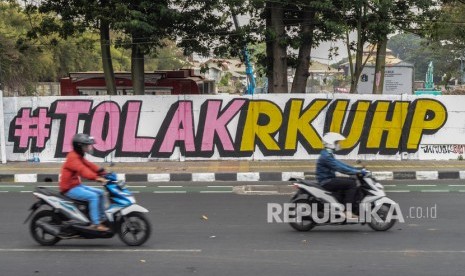 Sejumlah pengendara motor melintasi mural kritik sosial 'Tolak RUU KUHP' di Rawamangun, Jakarta Timur, Ahad (29/9/2019).