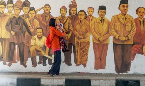 Warga melintas di depan mural bergambar tokoh Pahlawan Nasional di Jalan Raya Situ Cipayung, Jakarta Timur, Ahad (13/10/19). 