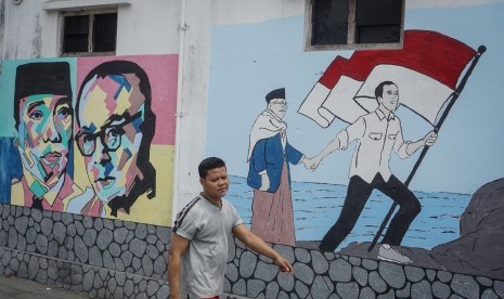 Warga melintas didepan mural bergambar Presiden dan Wakil Presiden terpilih Joko Widodo-Ma'ruf Amin di kampung Punggawan, Banjarsari, Solo, Jawa Tengah, Rabu (16/10/2019).