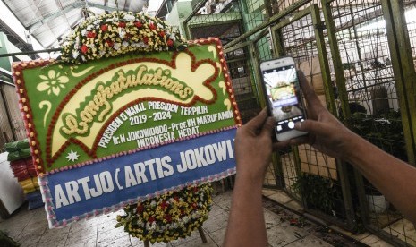 Pedagang mengabadikan karangan bunga ucapan selamat kepada Presiden terpilih Joko Widodo dan Wakil Presiden Ma’ruf Amin di Pasar Rawa Belong, Jakarta Barat, Sabtu (19/10/2019). 