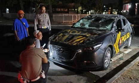 Polisi mengamati mobil dinas yang dirusak massa di halaman Stadion Mandala Krida Yogyakarta, Senin (21/10/2019).