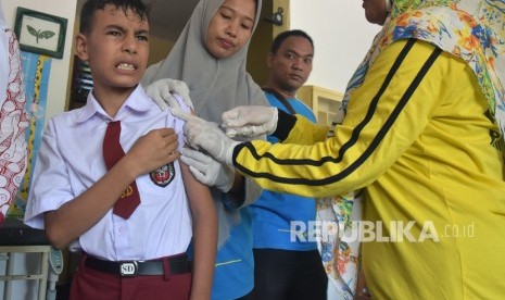 Seorang anak menahan sakit saat mendapat imunisasi. Isu kehalalan vaksin telah menurunkan angka anak yang diimunisasi.