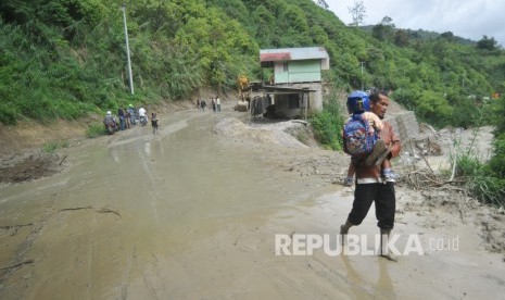 Pengendara meninggalkan motornya melewati jalan yang longsor (ilustrasi)