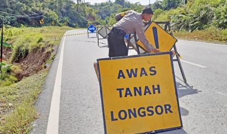 Seorang anggota Polsek Entikong memasang papan peringatan di lokasi jalan lintas negara yang mengalami retak akibat tanah longsor di perbatasan Entikong, Kabupaten Sanggau, Kalimantan Barat, Kamis (26/12/2019). 