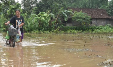 Warga menuntun sepedanya saat melintasi jalan yang terendam banjir di Kabupaten Madiun, Jawa Timur, Sabtu (28/12/2019).