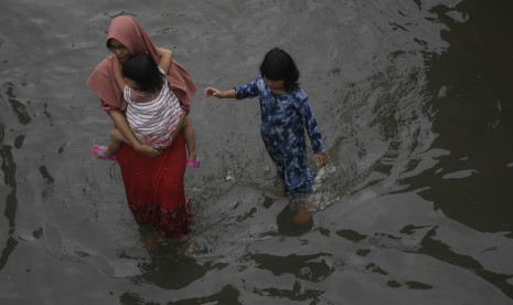 Warga melintasi banjir yang merendam Jalan Letjen S Parman dan tol dalam kota di Jakarta Barat, Rabu (1/1/2020). 