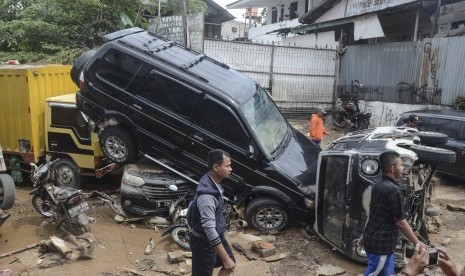 Sejumlah warga berjalan di dekat mobil yang rusak pascabanjir di Perumahan Pondok Gede Permai Bekasi, Jawa Barat, Kamis (2/1/2020). Pembangunan bendungan di Ciawi dan Sukamahi disebut bisa membantu atasi banjir Jabodetabek.