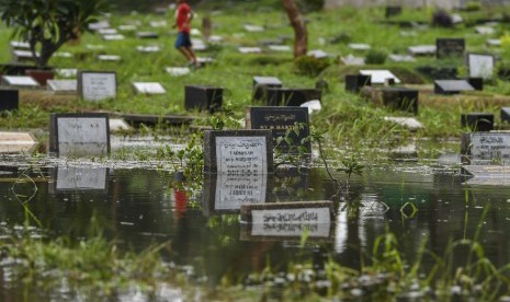 Warga melintas di area makam yang tergenang banjir di Taman Pemakaman Umum Tanah Kusir, Jakarta, Jumat (3/1/2020). 