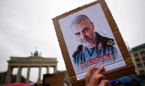 Seorang pemrotes memegang sebuah kardus yang memperlihatkan potret Letnan Jenderal Komandan Revolusioner Iran (IRGC) dan komandan Pasukan Quds Qassem Soleimani selama demonstrasi di depan Gerbang Brandenburg, dekat dengan kedutaan AS di Berlin, Jerman, 4 Januari 2020. Amerika Serikat telah mendeteksi pasukan rudal Iran pada kondisi siaga tinggi pascatewasnya Soleimani. 