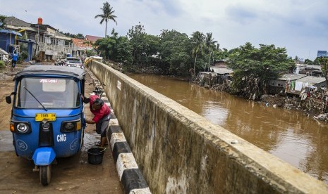 Warga membersihkan bajajnya di samping bantaran sungai Ciliwung di kawasan Bukit Duri, Jakarta, Ahad (5/1/2020).